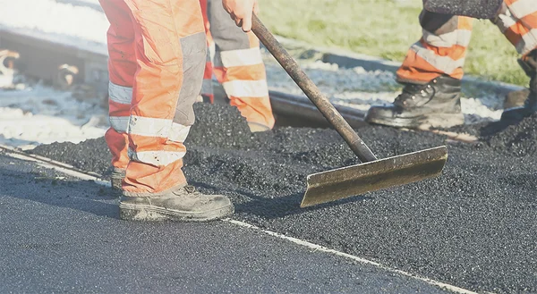 Asphalt wird mithilfe eines Werkzeugs glattgestrichen