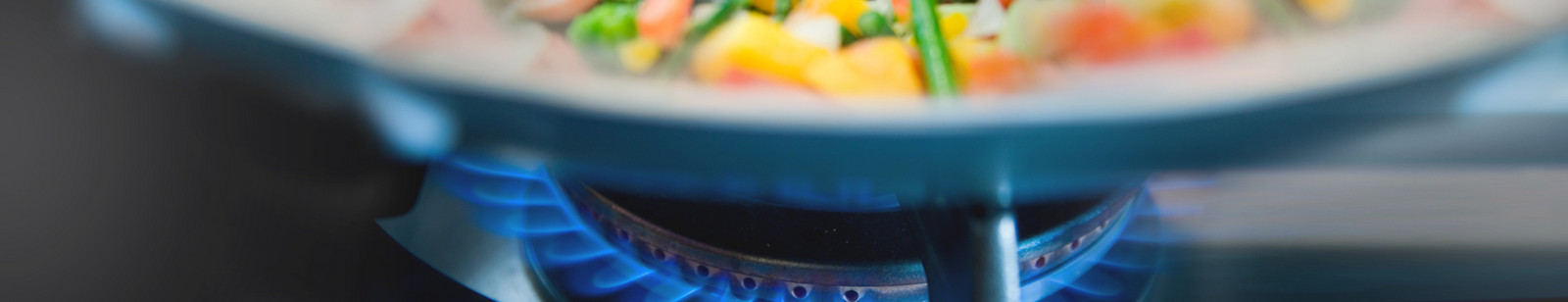 Nahaufnahme einer Gas-Herdflamme mit Topf in dem Gemüse erkennbar ist